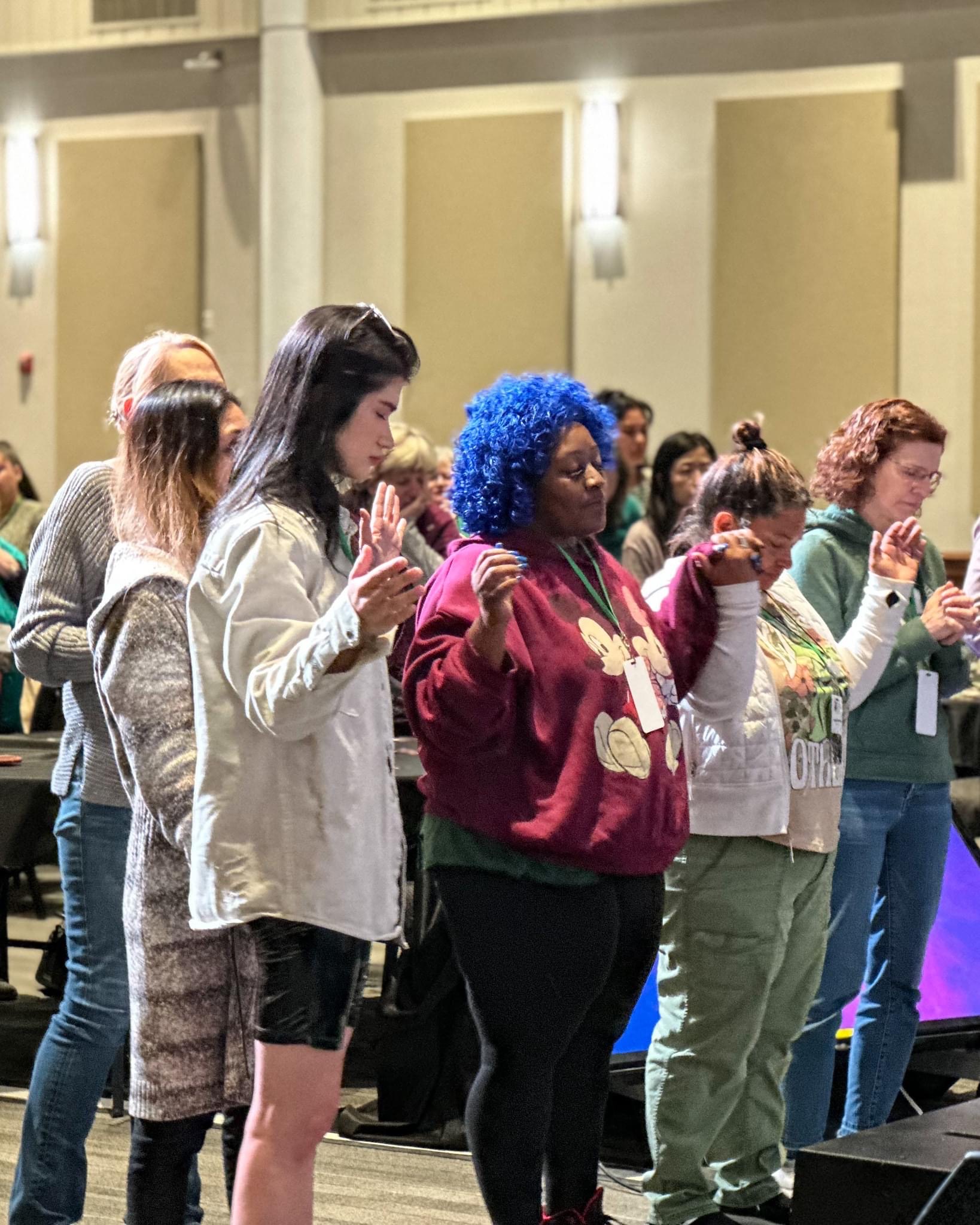 a group of women holding hands and praying together.